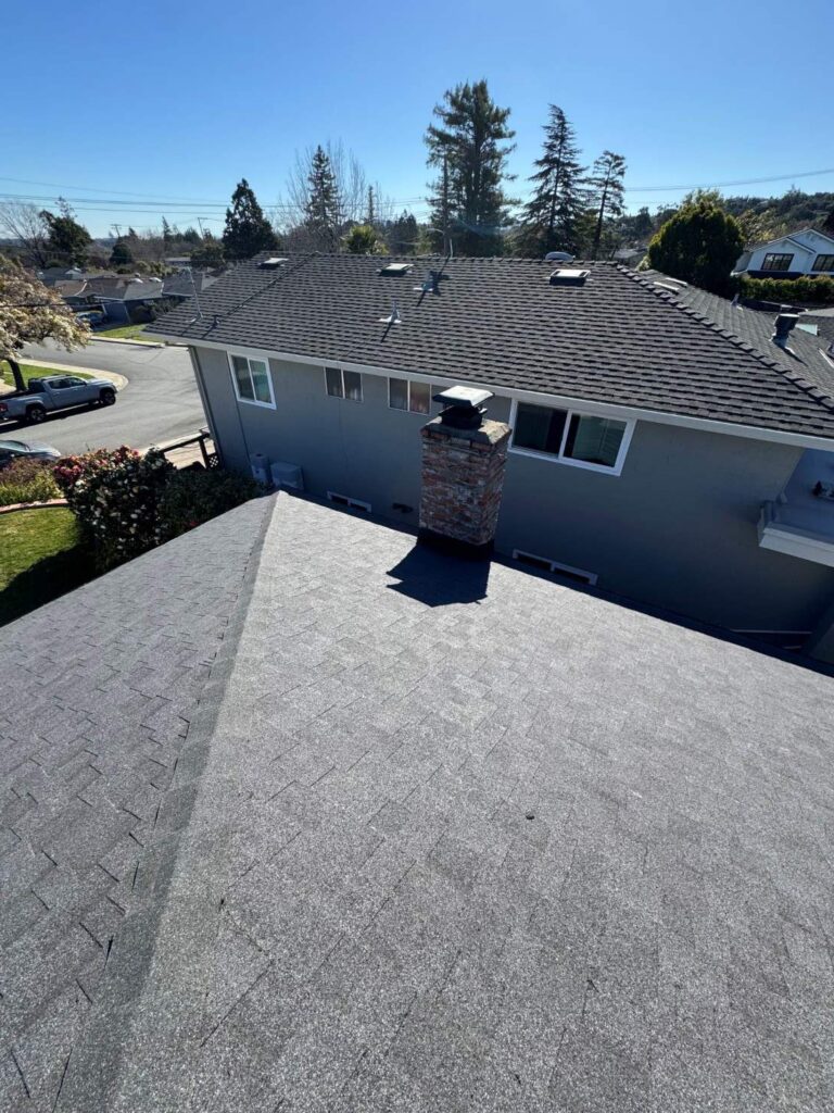 New asphalt shingle roof with chimney and attic vents on a residential home.