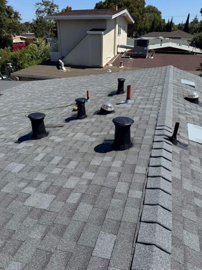 Newly installed gray asphalt shingle roof with multiple vent pipes and ridge cap shingles for ventilation and protection.