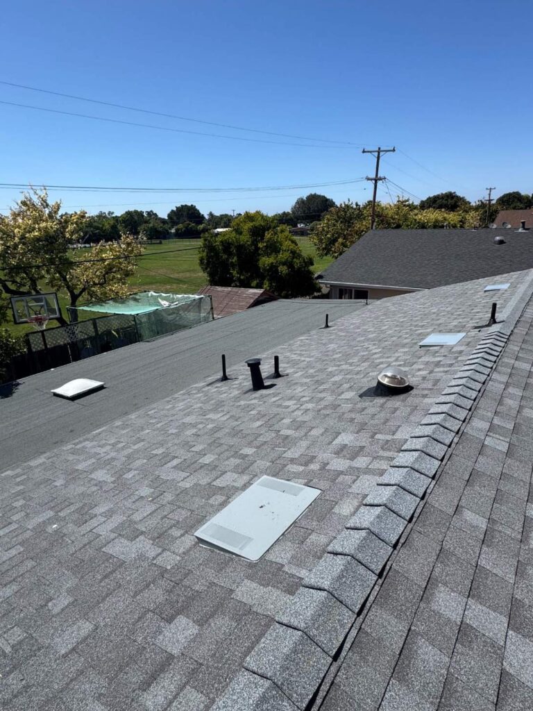New residential roof with gray asphalt shingles, ridge caps, and multiple ventilation systems installed.
