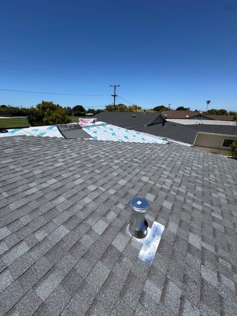 New asphalt shingle roof installation with metal vent pipe flashing and underlayment visible on adjacent section.