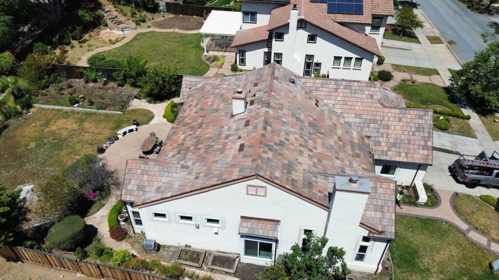 Aerial view of a residential home with a newly installed multi-colored tile roof, complete with chimney vents and landscaped backyard.