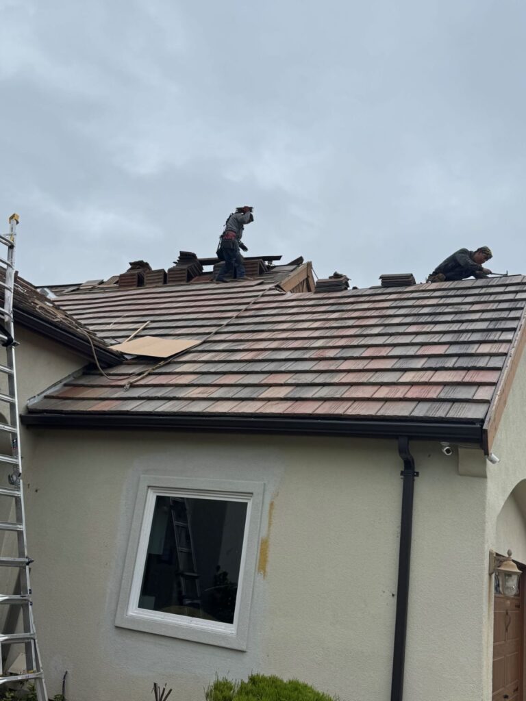 Roofers installing and repairing tile roofing on a residential home using safety gear and ladders.