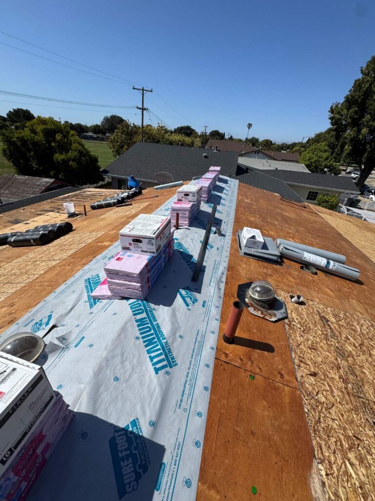 Residential roof replacement with synthetic underlayment installed and bundles of shingles staged for installation.