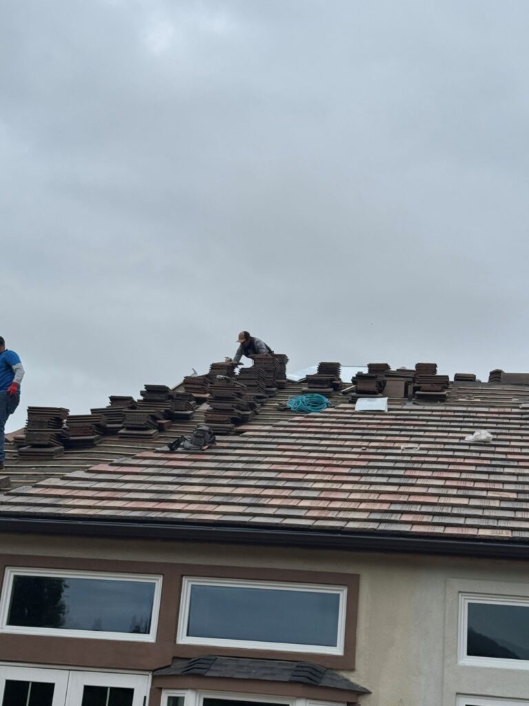 Roofing contractors stacking tiles during residential roof replacement on a two-story home.