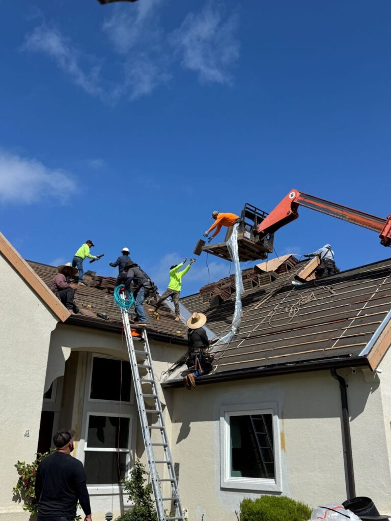 Roofing crew installing new tiles on a residential home using a ladder and lift for roof replacement.